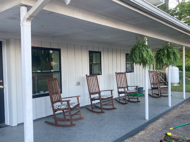Front porch with coated concrete floor, four wooden rocking chairs, and hanging ferns